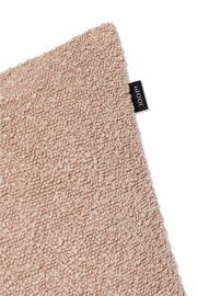 Nahaufnahme einer beigen Zierkissenhülle mit flauschiger Textur und einem kleinen schwarzen Etikett an der Seite.