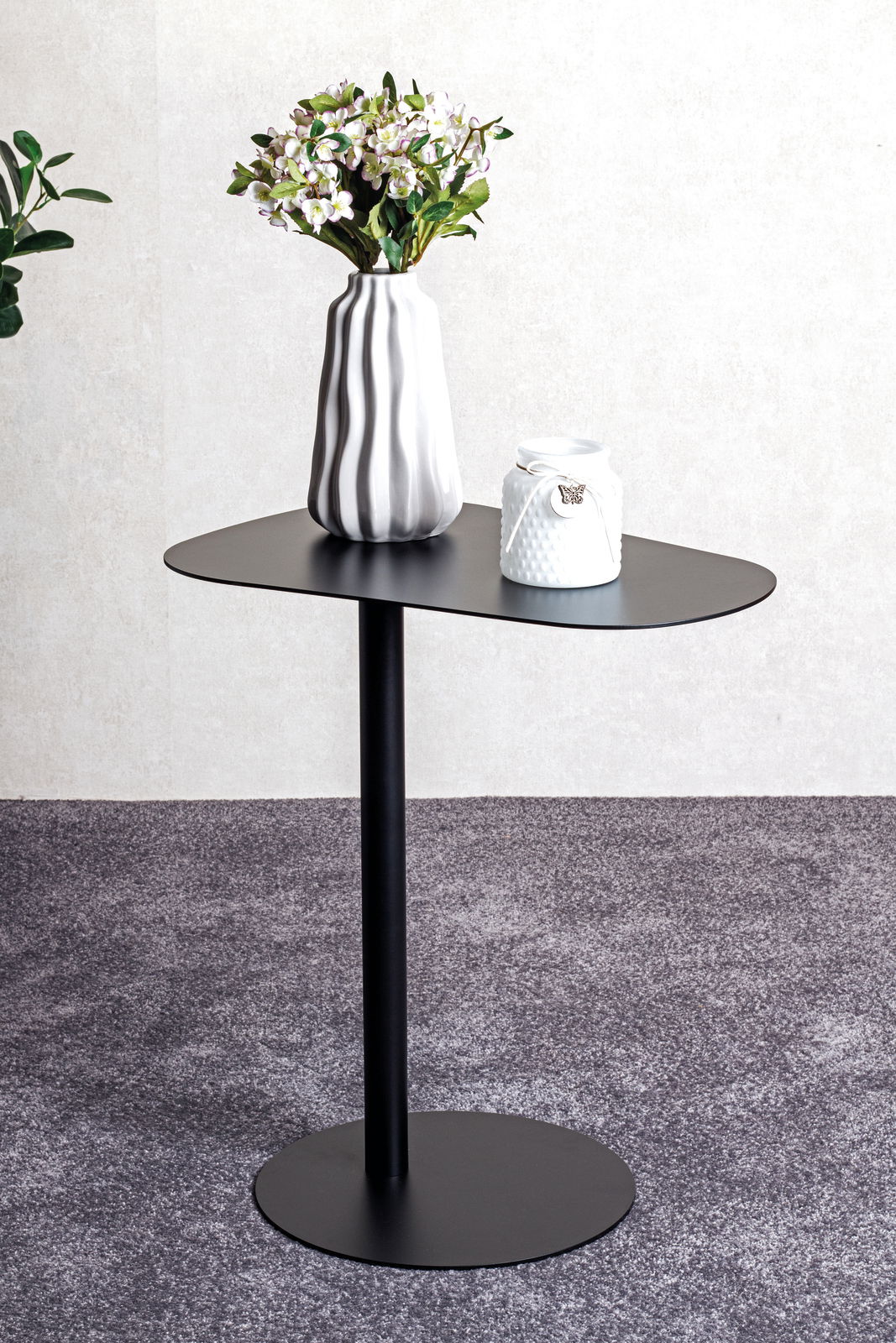 Moderner schwarzer Beistelltisch mit runder Platte und schlankem Standfuß, dekoriert mit einer Vase mit Blumen, seitliche Perspektive