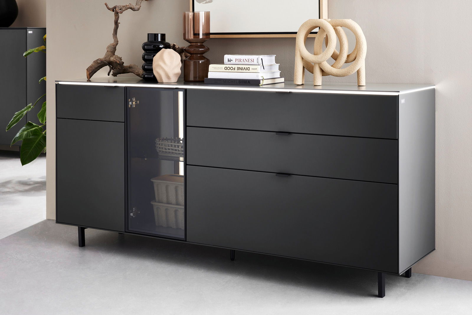 Modernes schwarzes Sideboard mit Schubladen und Glastür, dekoriert mit Büchern und Skulpturen, seitliche Perspektive