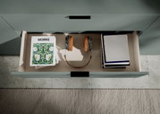 Offene Schublade eines Sideboards mit Büchern, Kopfhörern und Zeitschriften, von oben betrachtet.