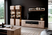 Moderne entertainmentset voor de woonkamer van licht hout, bestaande uit een tv-lowboard, twee verlichte glazen vitrinekasten en een wandplank voor een donkere muur, gefotografeerd van voren vanuit een licht zijdelings perspectief