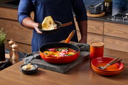 Sautepfanne 28cm in Ofenrot auf einem Küchentisch, gefüllt mit einem bunten Gericht, im Vordergrund aus der Vogelperspektive.