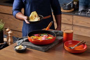 Sautepfanne 28cm in Ofenrot auf einem Küchentisch, gefüllt mit einem bunten Gericht, im Vordergrund aus der Vogelperspektive.