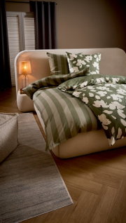 Grün-weißes Bettwäsche-Set mit Streifen- und Blumenmuster auf cremefarbenem Polsterbett im Schlafzimmer, Perspektive: schräg von vorne/seitlich
