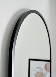 Nahaufnahme eines ovalen Spiegels mit schwarzem Rahmen, seitliche Perspektive.