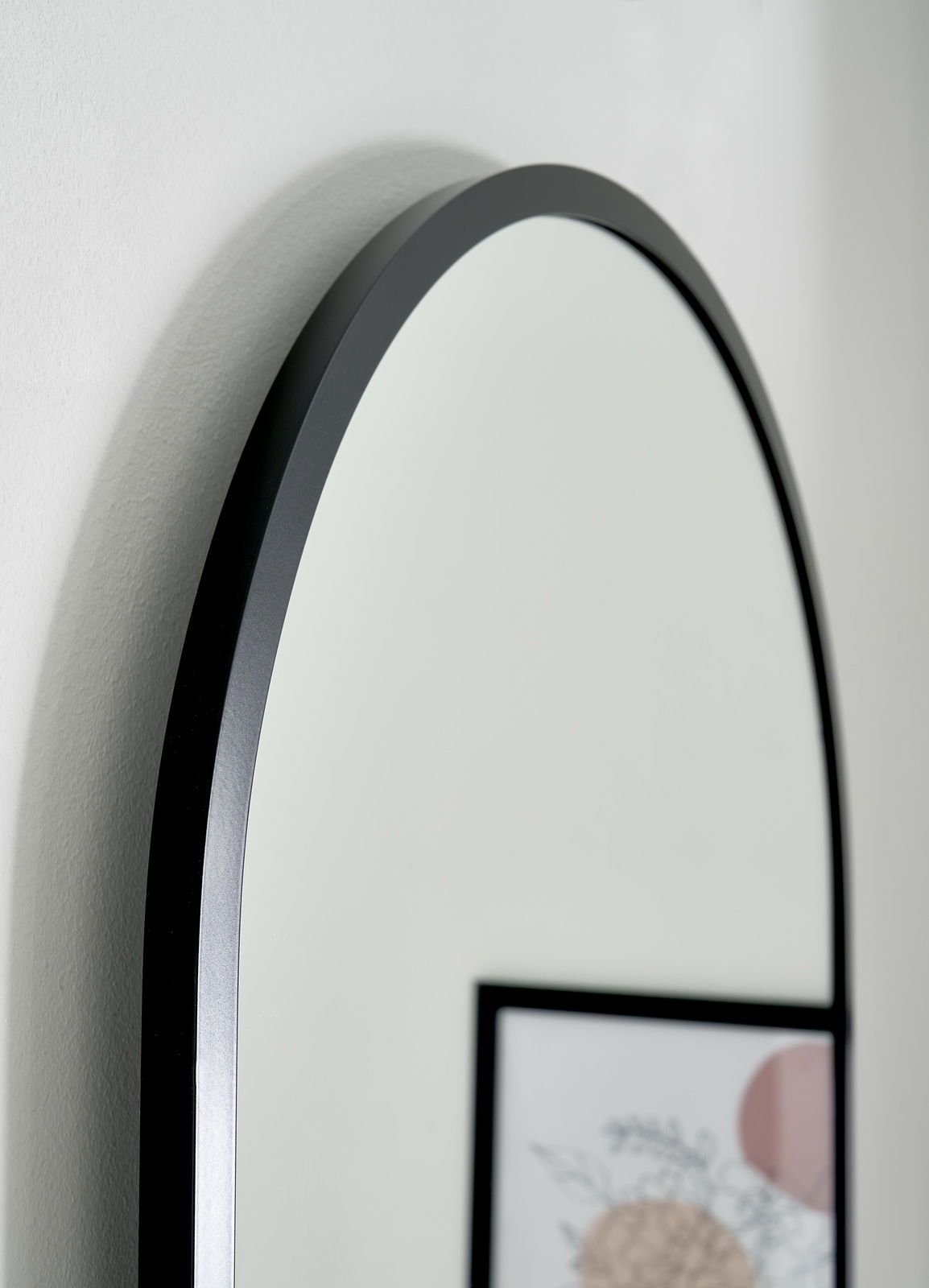 Nahaufnahme eines ovalen Spiegels mit schwarzem Rahmen, seitliche Perspektive.