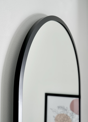 Nahaufnahme eines ovalen Spiegels mit schwarzem Rahmen, seitliche Perspektive.