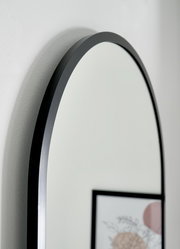 Nahaufnahme eines ovalen Spiegels mit schwarzem Rahmen, seitliche Perspektive.