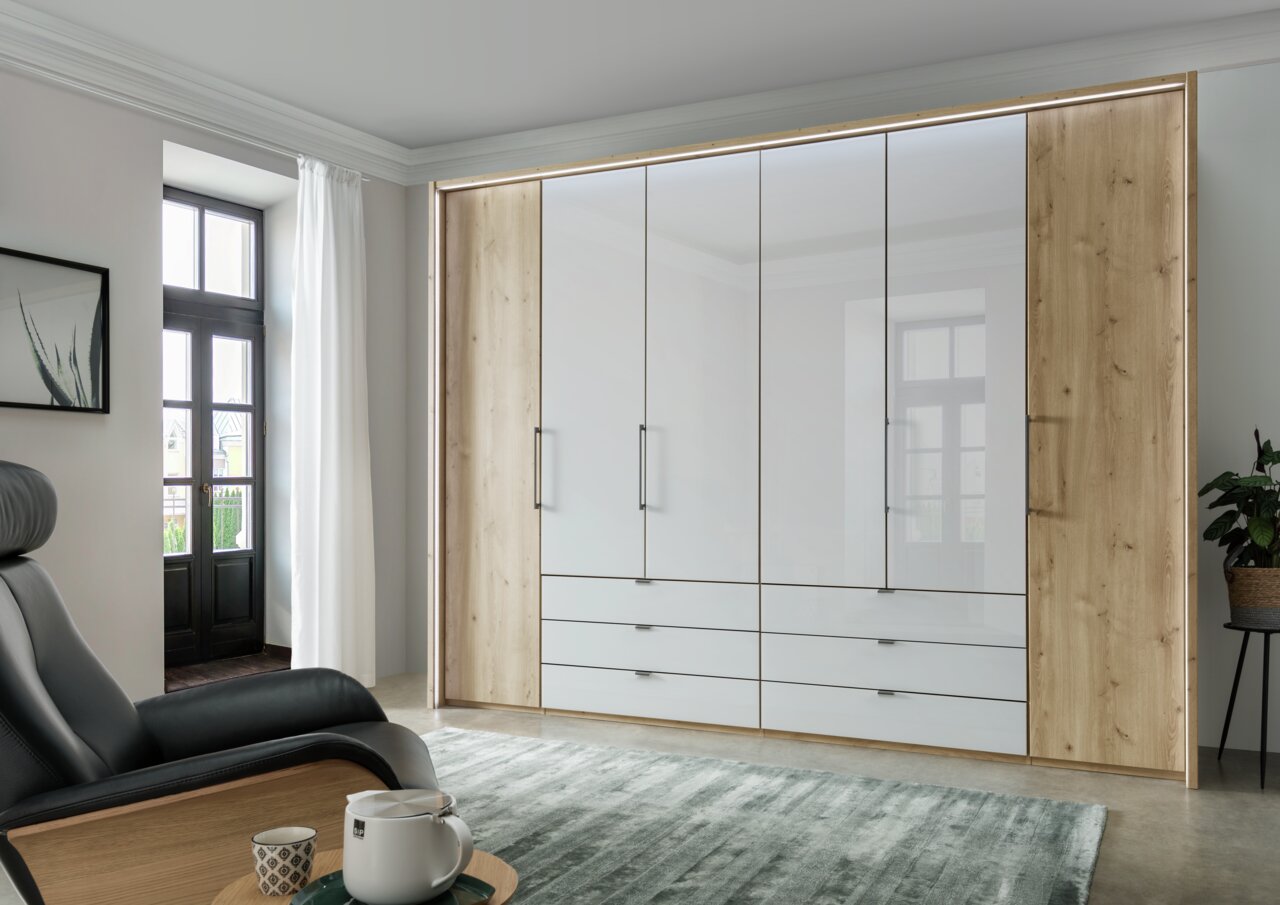Moderner 6-türiger Falttürenschrank in Holzoptik mit weißen Fronten, frontal fotografiert in einem stilvoll eingerichteten Raum.