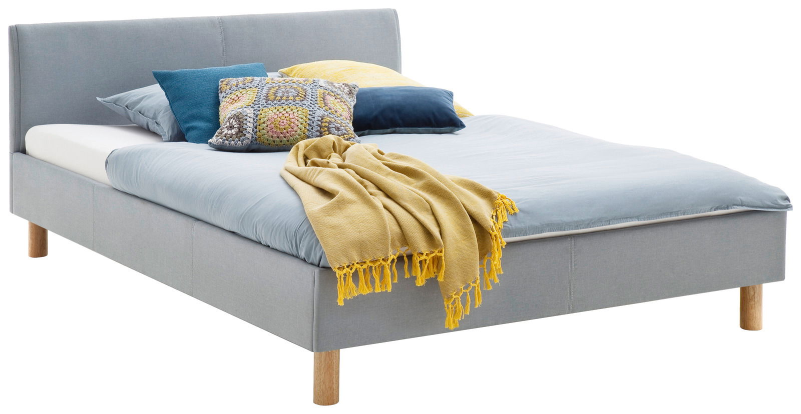 Graues Polsterbett mit Holzfüßen, dekoriert mit bunten Kissen und einer gelben Decke, seitliche Perspektive