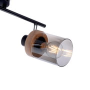 Moderne Decken-Spotleuchte mit schwarzer Schiene, Holzdetails und zylindrischem Rauchglas-Schirm mit sichtbarer LED-Filamentlampe, schräg von unten aus seitlicher Nahaufnahme fotografiert