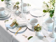 Festlich gedeckter Tisch mit weißem Porzellangeschirr, Kristallgläsern, goldfarbenem Besteck, Kerzenständern und weiß-grüner Blumendeko, aus schräger Vogelperspektive von oben fotografiert