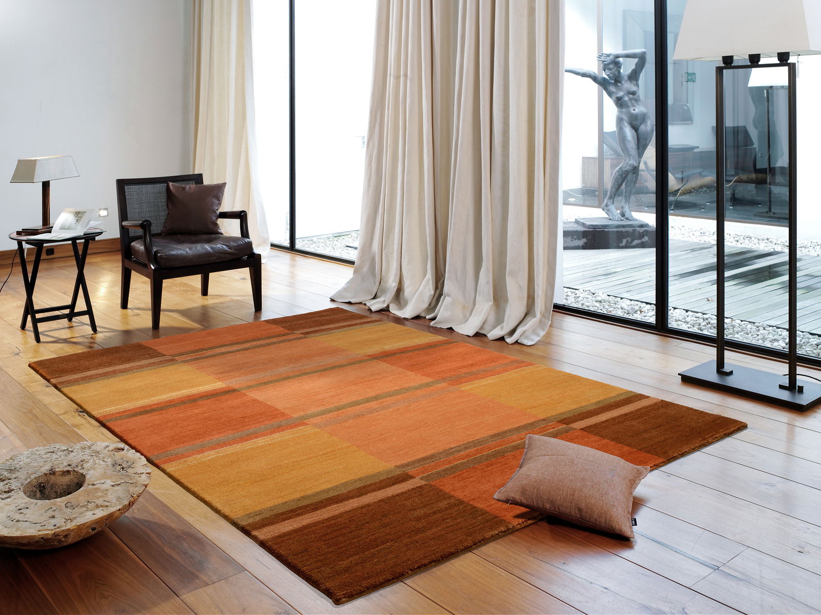 Moderner Teppich in warmen Orangetönen auf Holzboden in einem stilvollen Wohnzimmer mit großen Fenstern und eleganter Einrichtung, aus der Vogelperspektive.