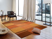 Moderner Teppich in warmen Orangetönen auf Holzboden in einem stilvollen Wohnzimmer mit großen Fenstern und eleganter Einrichtung, aus der Vogelperspektive.