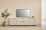 Modernes weißes TV-Lowboard mit zwei Schubladen und seitlichen Türen, darauf ein Flachbildfernseher; Frontansicht in minimalistischer Wohnraum-Szene mit Pflanze links und Deko rechts