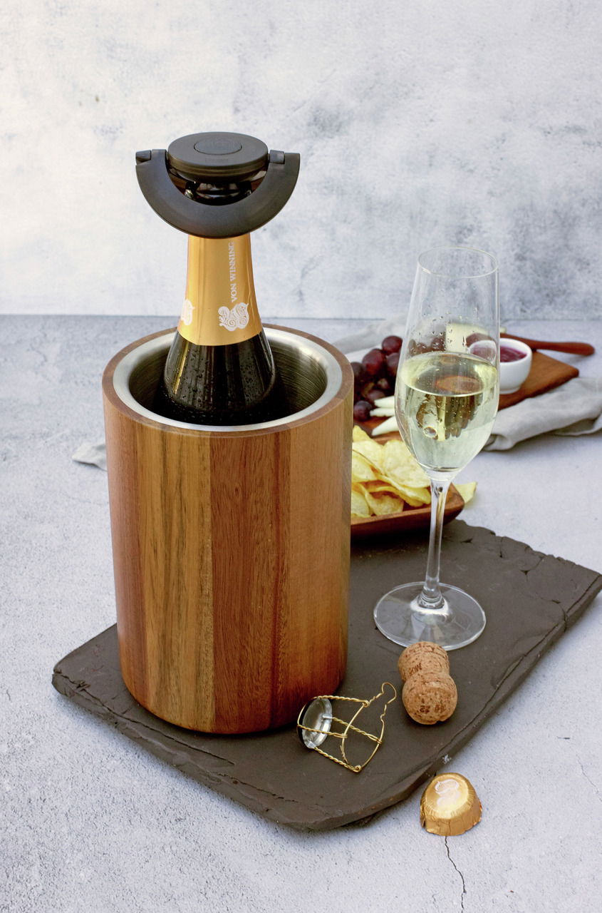 Holz-Weinkühler mit Sektflasche, seitliche Perspektive, daneben ein gefülltes Sektglas und Snacks.