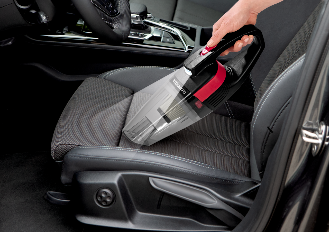 Akku Handstaubsauger in der Hand, der auf einem Autositz verwendet wird, seitliche Perspektive