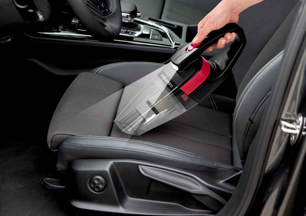 Akku Handstaubsauger in der Hand, der auf einem Autositz verwendet wird, seitliche Perspektive