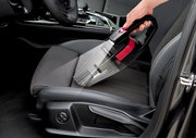 Akku Handstaubsauger in der Hand, der auf einem Autositz verwendet wird, seitliche Perspektive