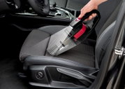 Akku Handstaubsauger in der Hand, der auf einem Autositz verwendet wird, seitliche Perspektive