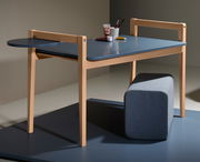 Tischplatte Tiny Table in seitlicher Perspektive mit blauer Oberfläche und hellem Holzrahmen, ergänzt durch eine runde Ablagefläche und einen grauen Hocker.