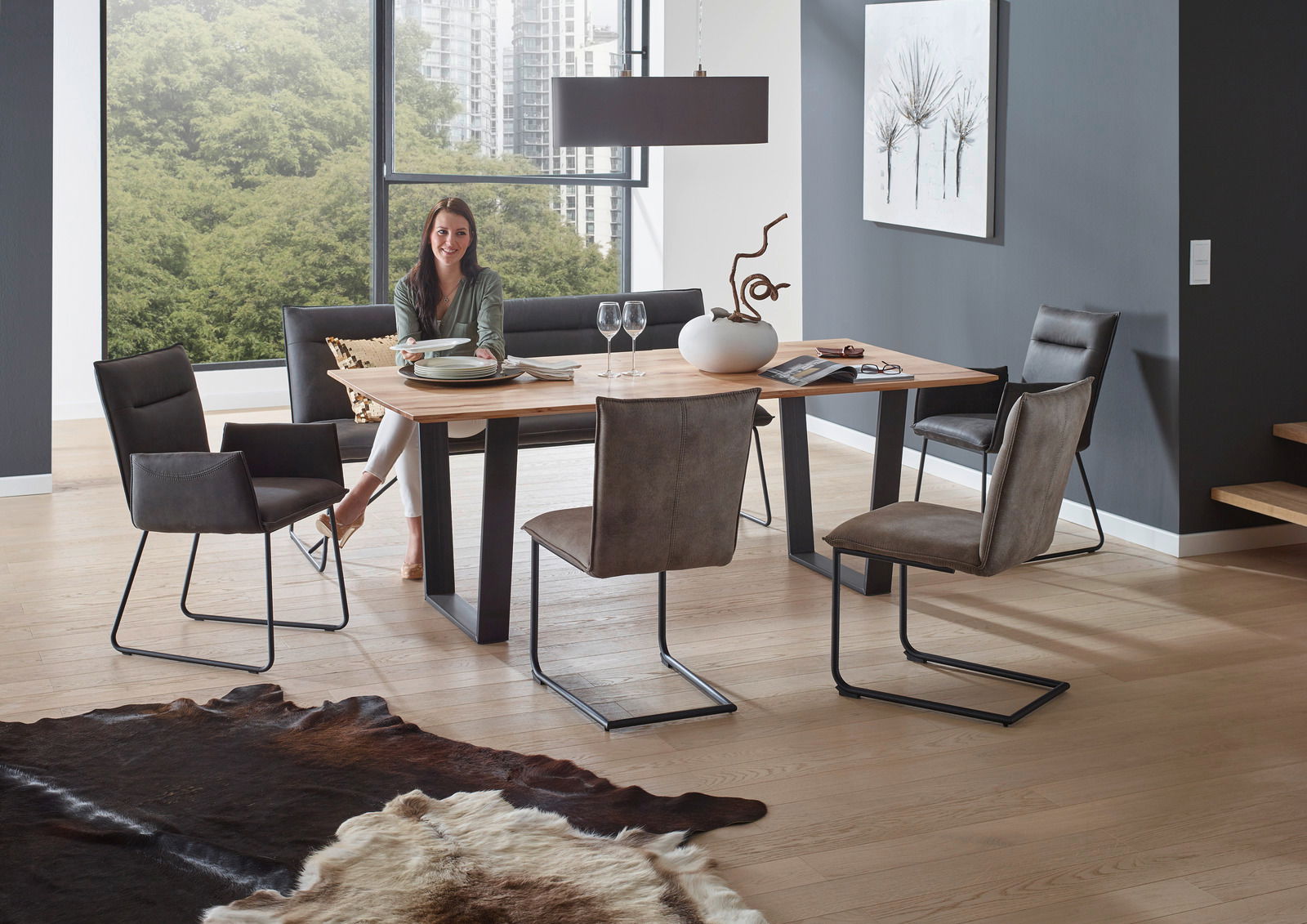Moderner Esstisch mit Holzplatte und schwarzen Metallbeinen, umgeben von stilvollen Stühlen in einem hellen Raum mit großen Fenstern, seitliche Perspektive.