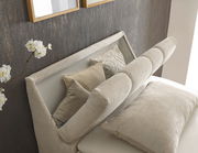 Nahaufnahme eines eleganten Boxspringbetts mit beigen Kissen und einem gepolsterten Kopfteil, seitliche Perspektive.