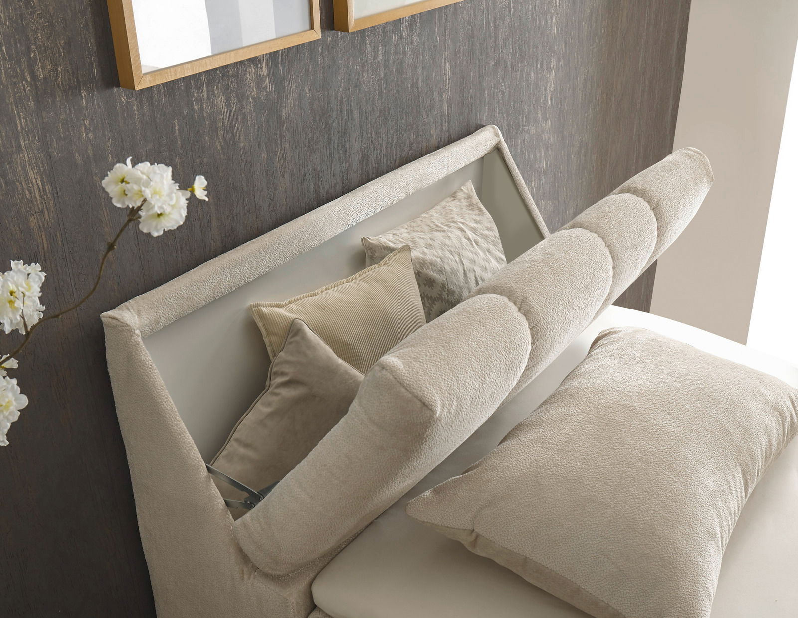 Nahaufnahme eines eleganten Boxspringbetts mit beigen Kissen und einem gepolsterten Kopfteil, seitliche Perspektive.