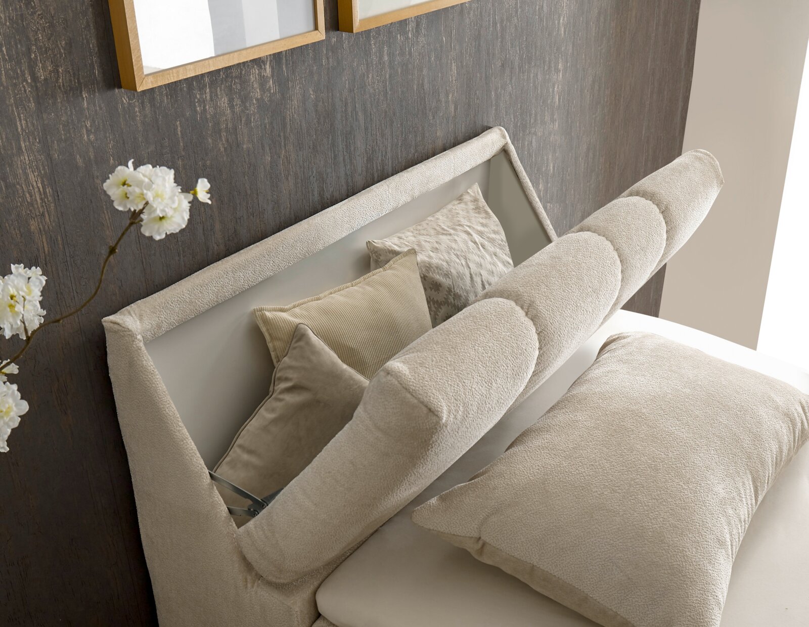 Nahaufnahme eines eleganten Boxspringbetts mit beigen Kissen und einem gepolsterten Kopfteil, seitliche Perspektive.