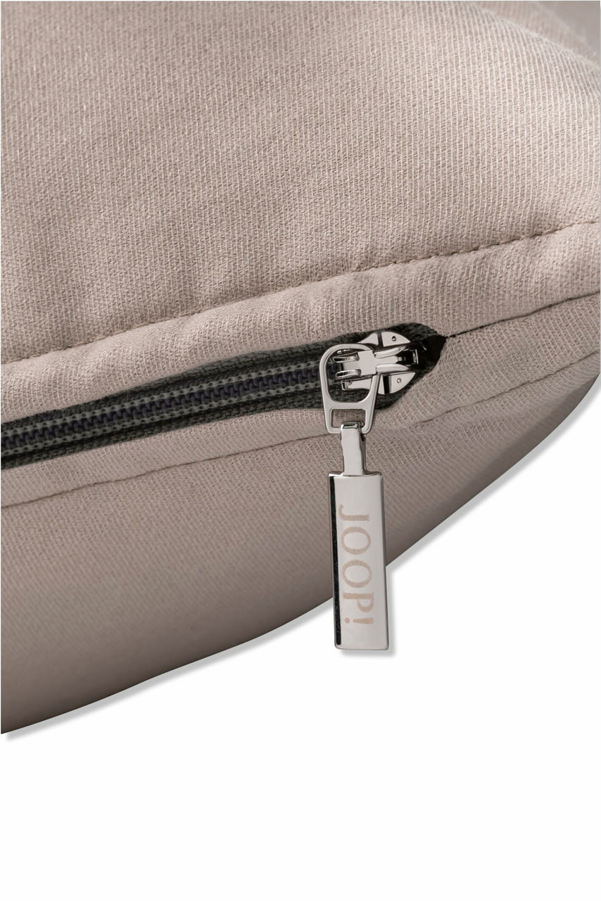 Nahaufnahme einer beigen Zierkissenhülle mit Reißverschluss und einem Anhänger mit der Aufschrift 'JOOP!'