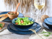 Elegantes Tellerset in Blau mit Salat und Tomaten, von oben betrachtet, auf einem gedeckten Tisch mit Weinglas und Holzschale.