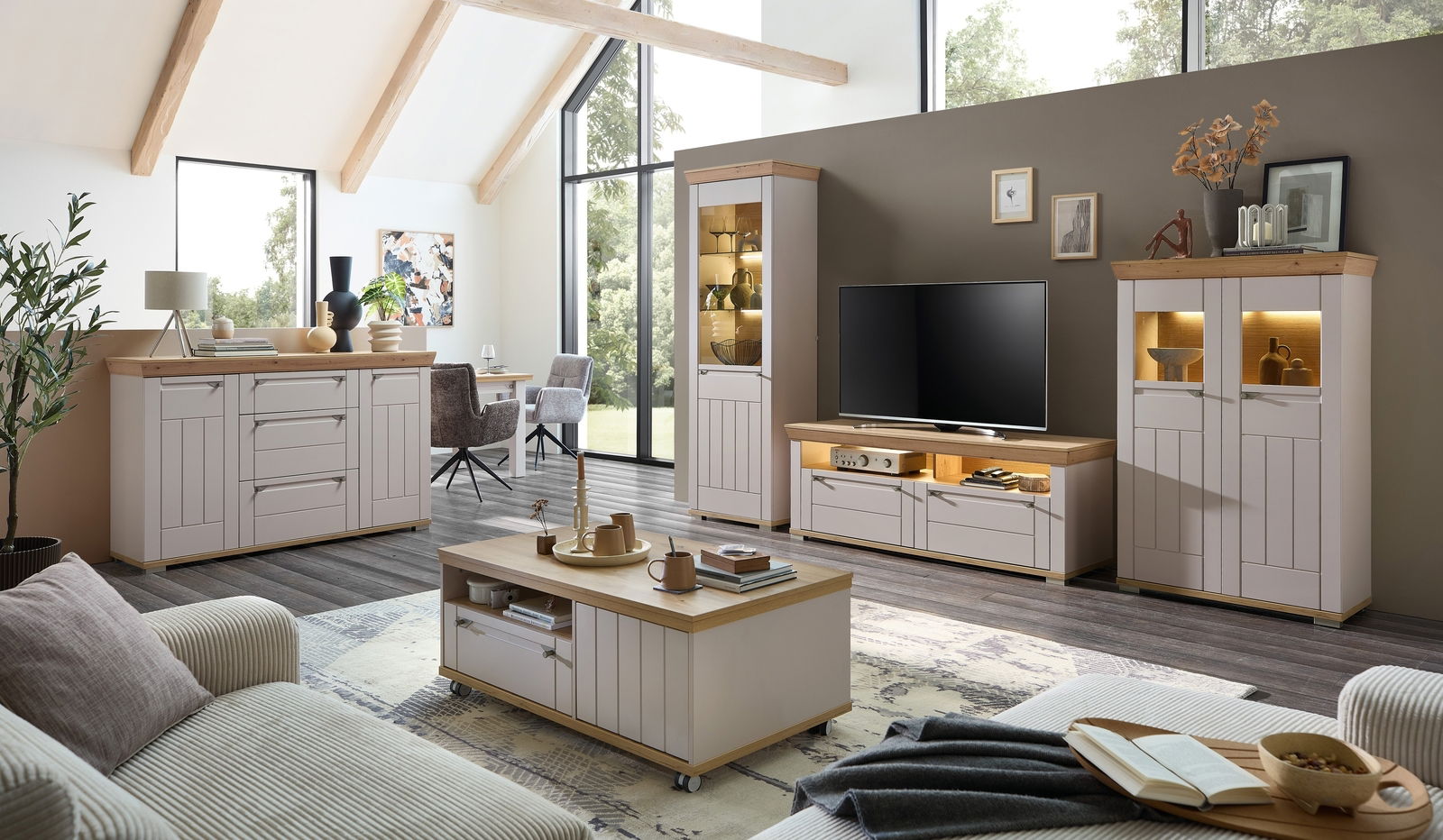 Moderne Wohnzimmer-Wandkombination in hellem Holz und Weiß, bestehend aus TV-Schrank, Vitrinen und Sideboard, in einem hellen Raum mit großen Fenstern, aus der Perspektive eines gemütlichen Wohnzimmers.