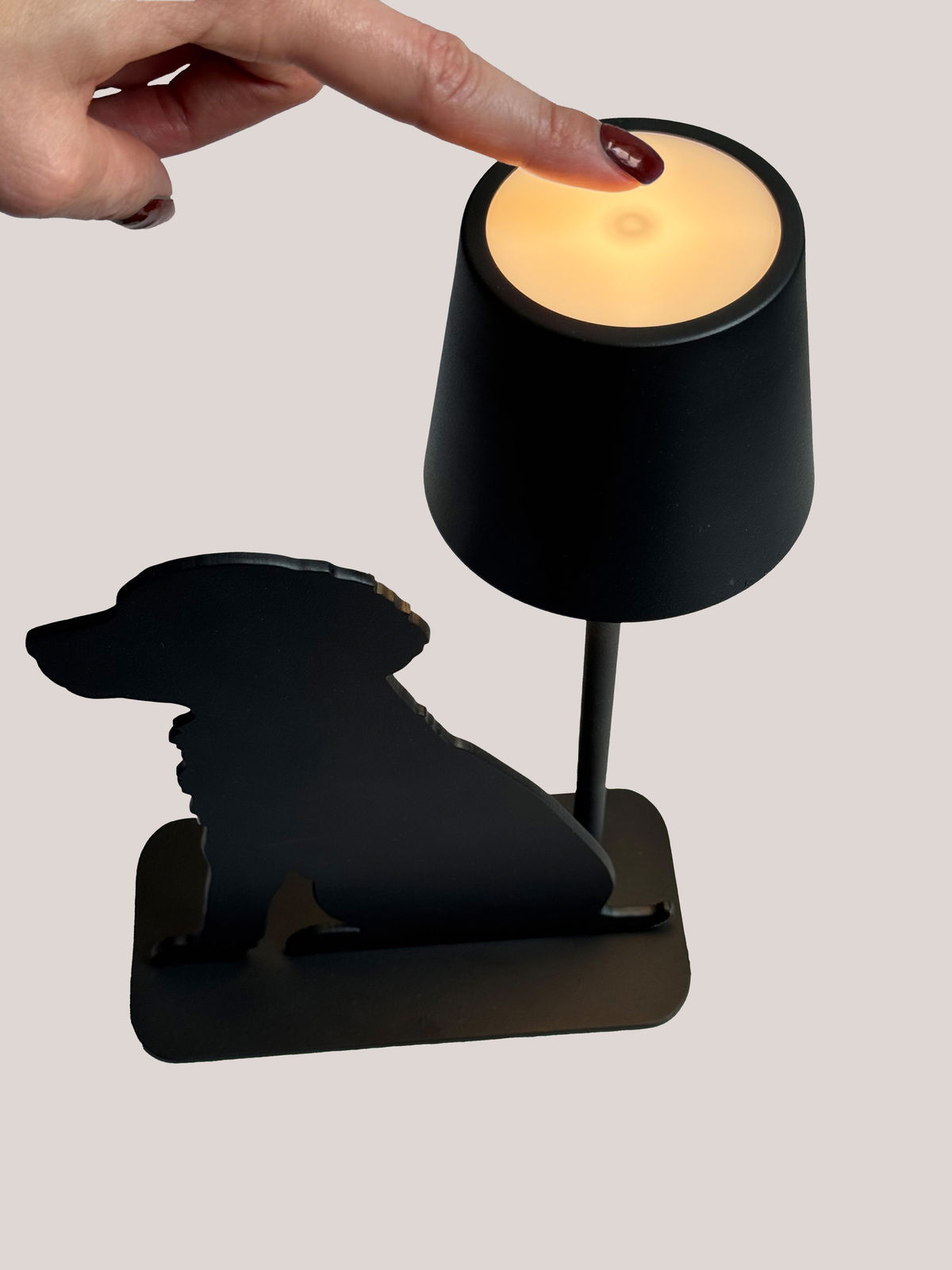 Akku-Tischleuchte mit Hundesilhouette, seitliche Perspektive, Finger berührt die Oberseite der Lampe.