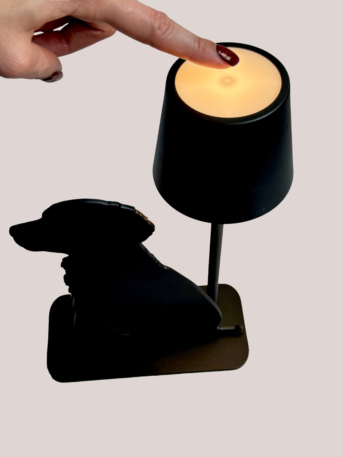 Akku-Tischleuchte mit Hundesilhouette, seitliche Perspektive, Finger berührt die Oberseite der Lampe.