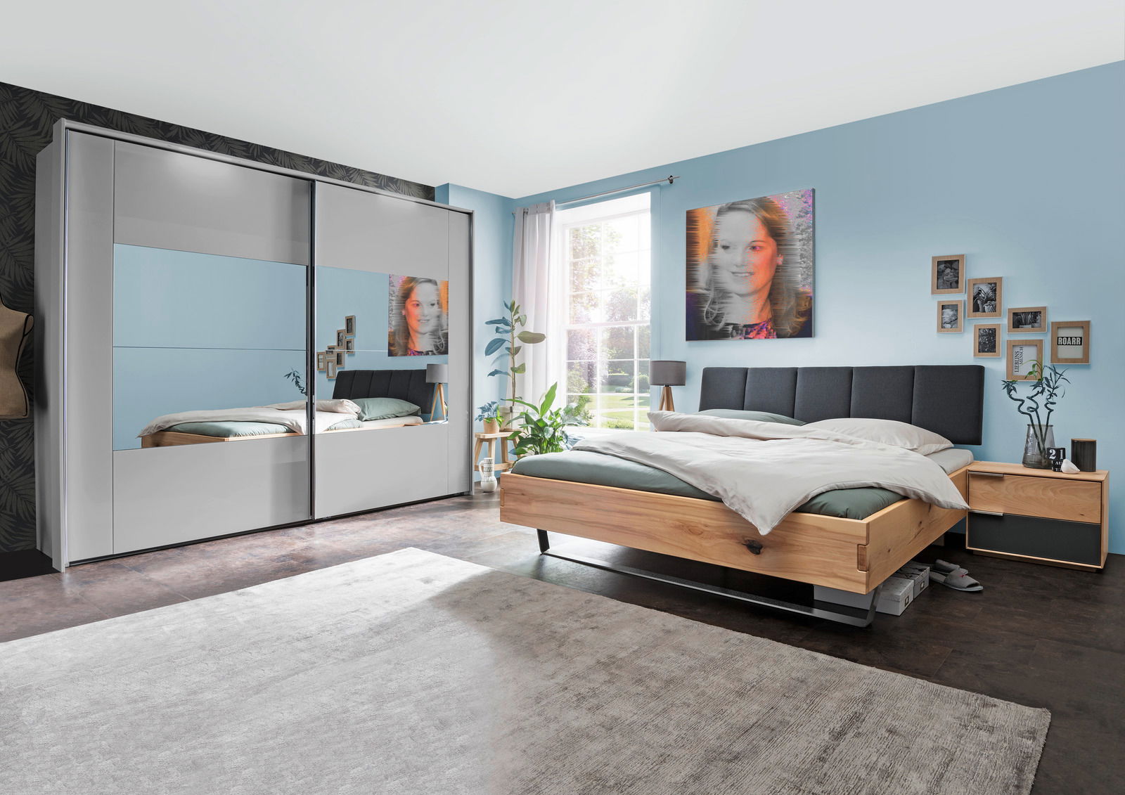 Schlafzimmer mit modernem Schwebetürenschrank in Weiß mit Spiegeln, daneben ein Bett mit Holzrahmen und grauem Kopfteil, seitliche Perspektive.