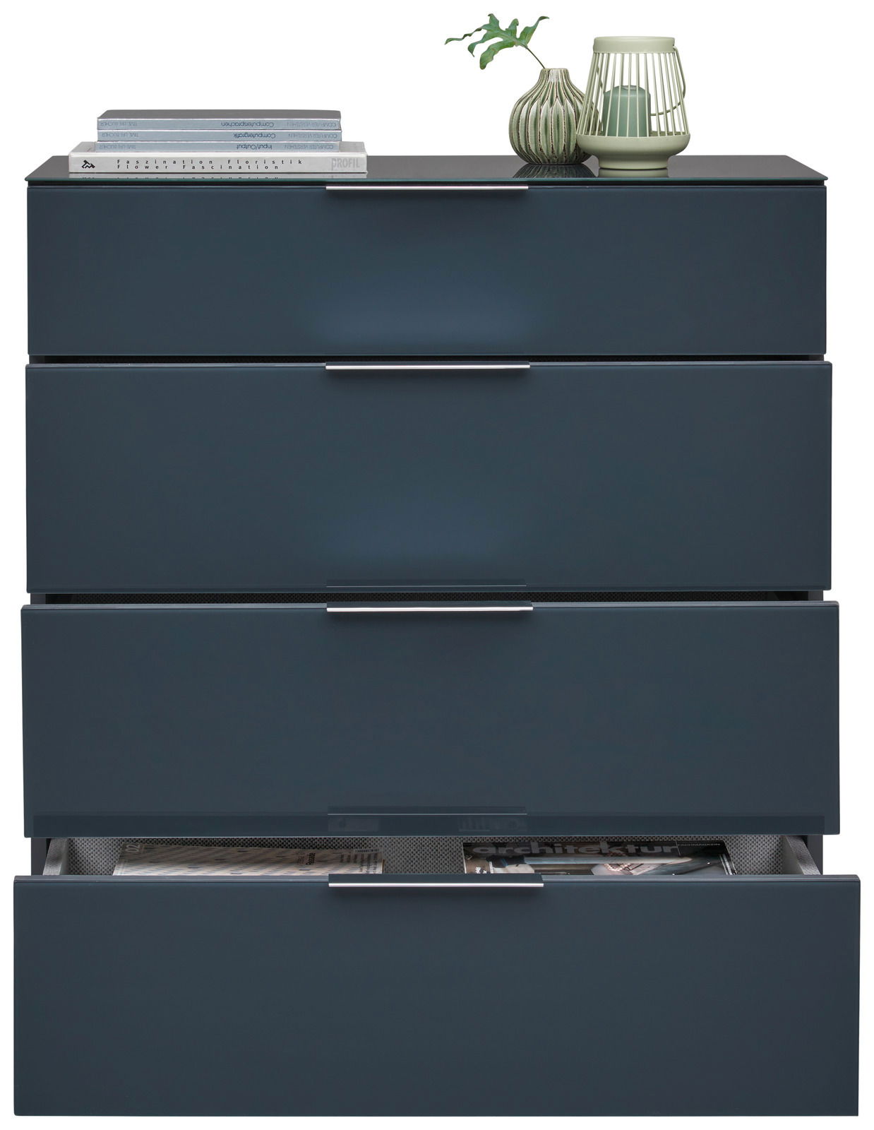 Schubkastenkommode in dunklem Blau mit vier Schubladen, teilweise geöffnet, aus frontaler Perspektive. Dekoriert mit Büchern und einer Vase auf der Oberseite.