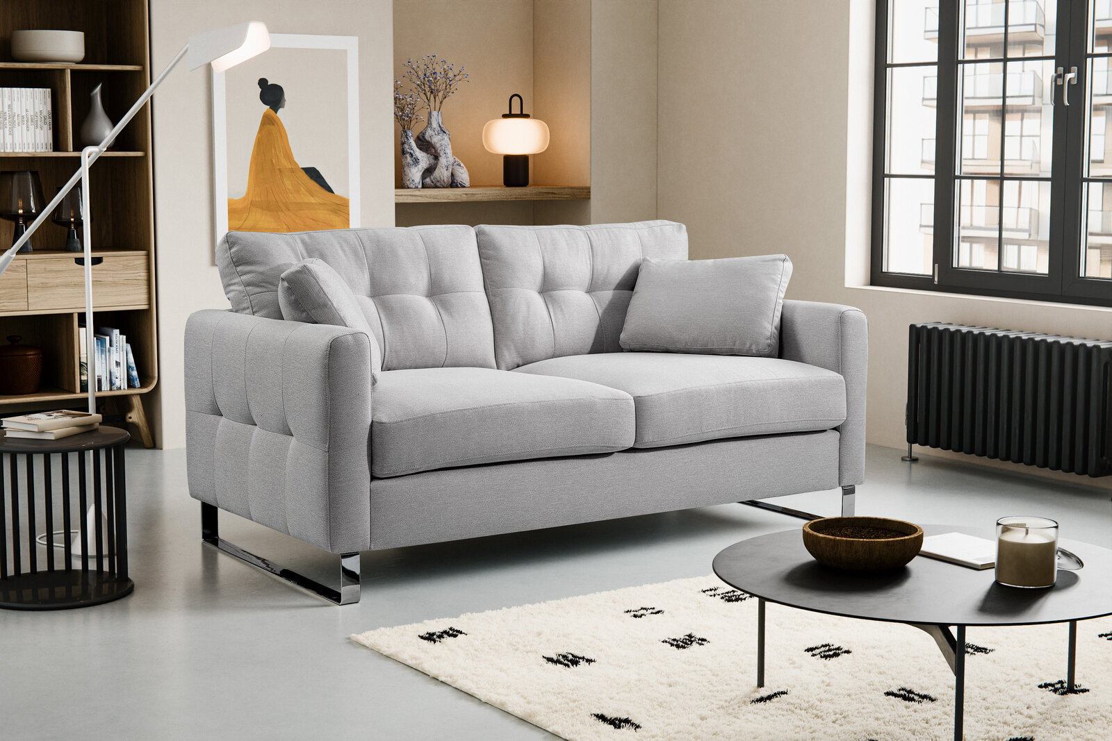 Modernes hellgraues 2-Sitzer-Sofa mit gesteppter Rückenlehne, breiten Armlehnen und verchromten Kufenfüßen im Wohnzimmer, schräg von vorne links fotografiert