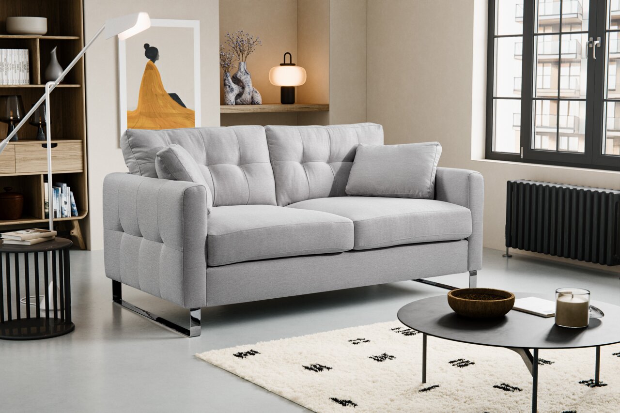 MID.YOU 2 Sitzer HERA Modernes hellgraues 2-Sitzer-Sofa mit gesteppter Rückenlehne, breiten Armlehnen und verchromten Kufenfüßen im Wohnzimmer, schräg von vorne links fotografiert