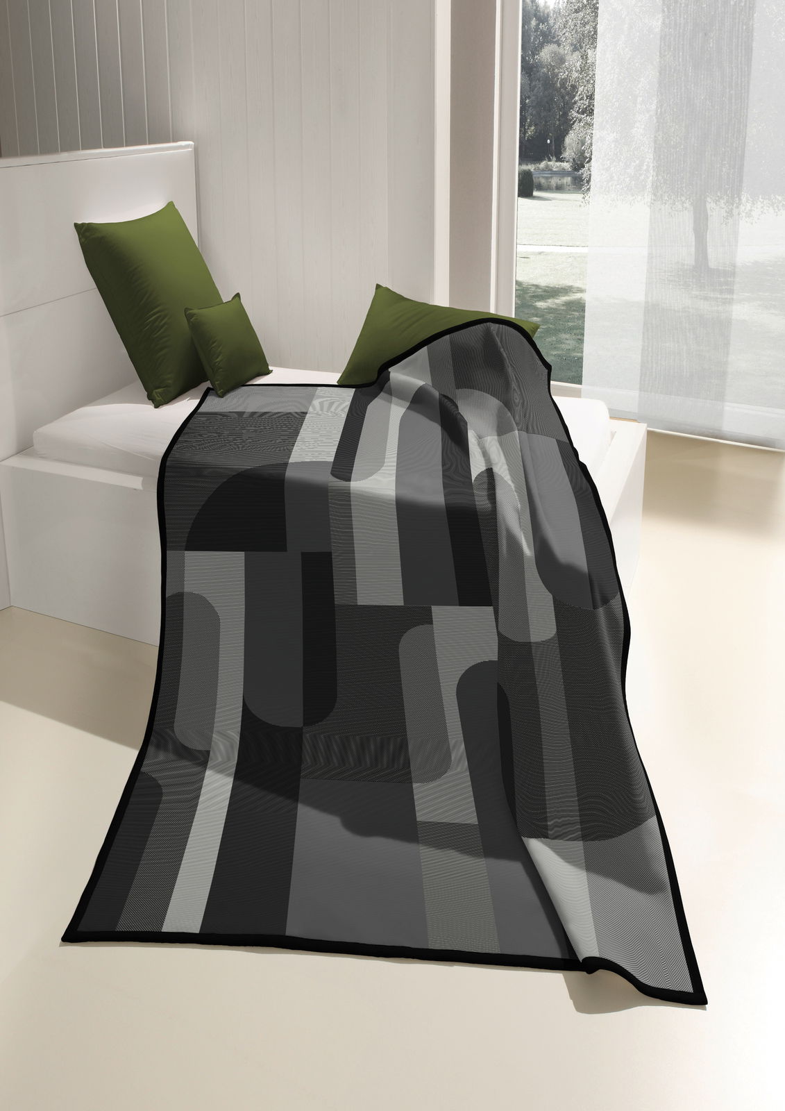 biederlack Wohndecke COTTON HOME Moderne Wohndecke in Grautönen mit geometrischem Muster, drapiert auf einem Bett mit grünen Kissen, seitliche Perspektive.