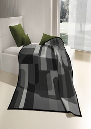 Moderne Wohndecke in Grautönen mit geometrischem Muster, drapiert auf einem Bett mit grünen Kissen, seitliche Perspektive.