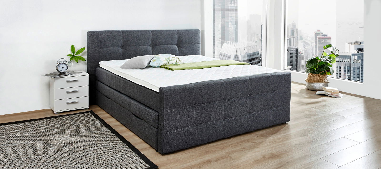 Graues Boxspringbett in modernem Schlafzimmer mit Stadtblick, seitliche Perspektive