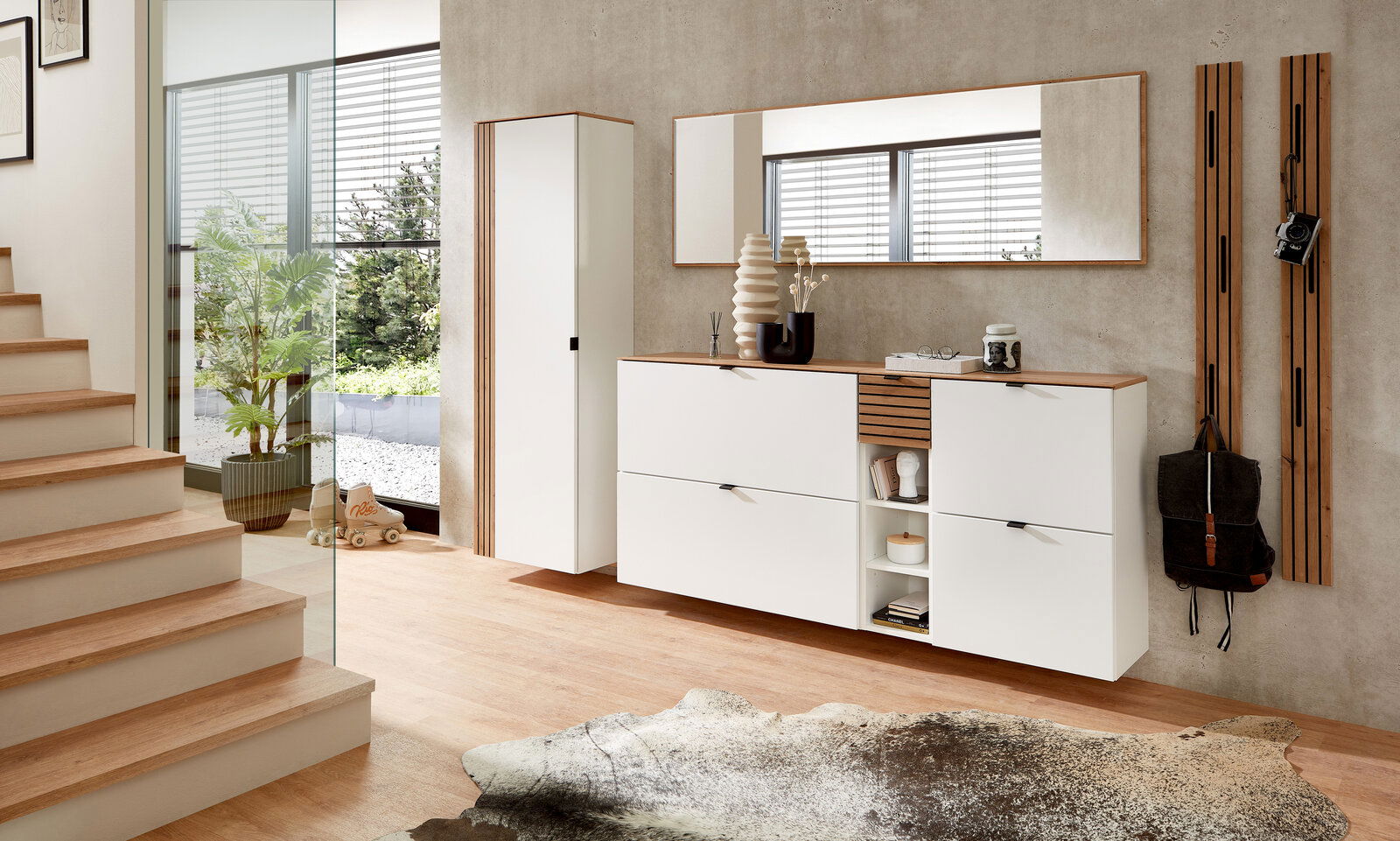 Voleo Hänge-Schuhschrank breit DIANA Moderne Garderobeneinrichtung mit weißem Hängeschrank, schmalem Spiegel und Garderobenpaneel in einem hellen Raum, seitliche Perspektive.