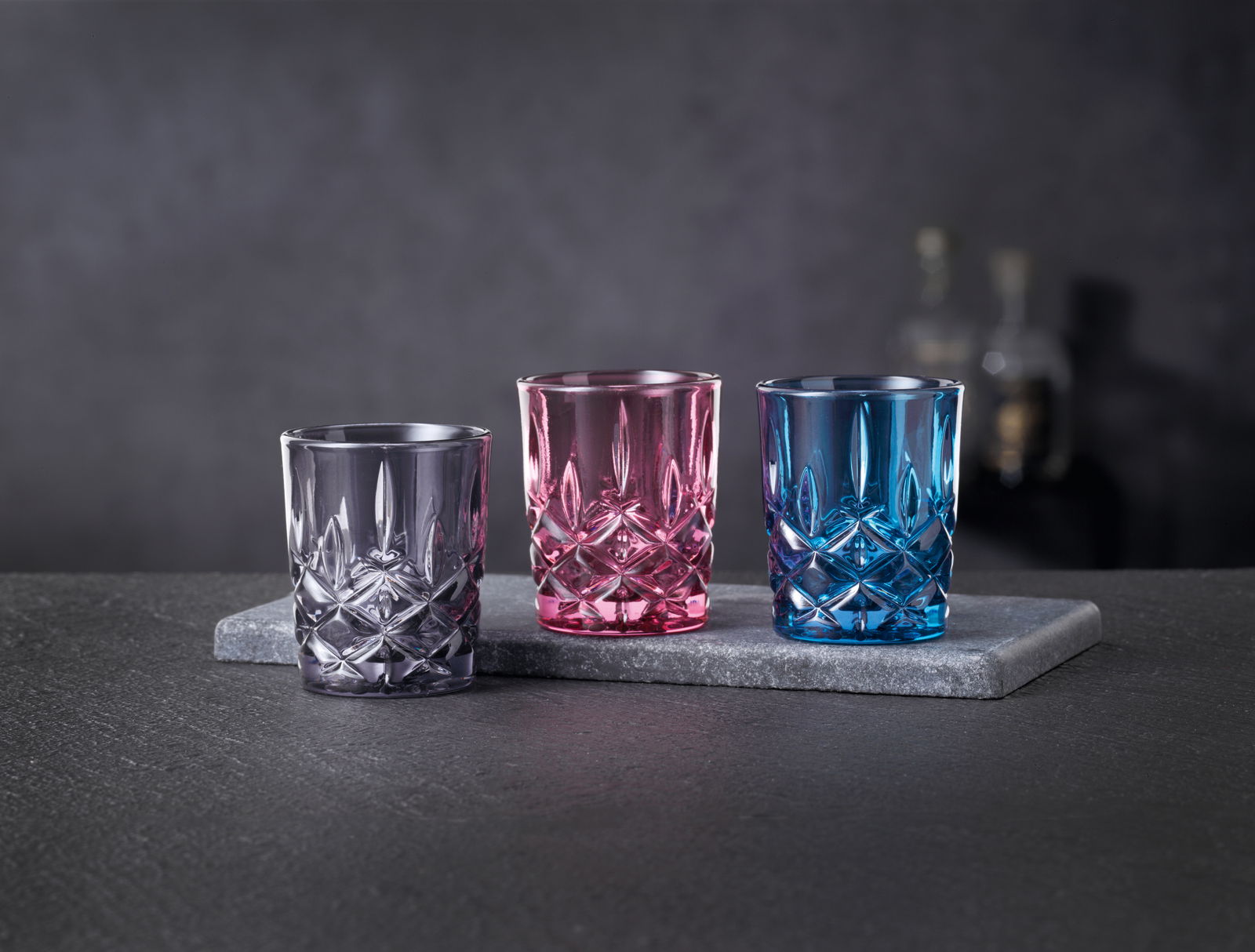 Nachtmann Stampler-Set 3 tlg. NOBLESSE Drei bunte Stamper-Gläser in Lila, Pink und Blau auf einer grauen Steinplatte, seitliche Perspektive.