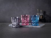 Drei bunte Stamper-Gläser in Lila, Pink und Blau auf einer grauen Steinplatte, seitliche Perspektive.