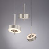 Drei moderne Pendelleuchten Q-ROTATE in gebürstetem Metall, aus seitlicher Perspektive fotografiert, mit kreisförmigem Design und warmem Licht.
