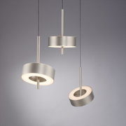 Drie moderne hanglampen van het type Q-ROTATE in geborsteld metaal, gefotografeerd vanuit een zijdelingse hoek, met een cirkelvormig ontwerp en warm licht.