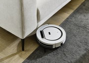 Weißer Saugroboter reinigt den Boden neben einer hellen Eckgarnitur, Perspektive von oben.