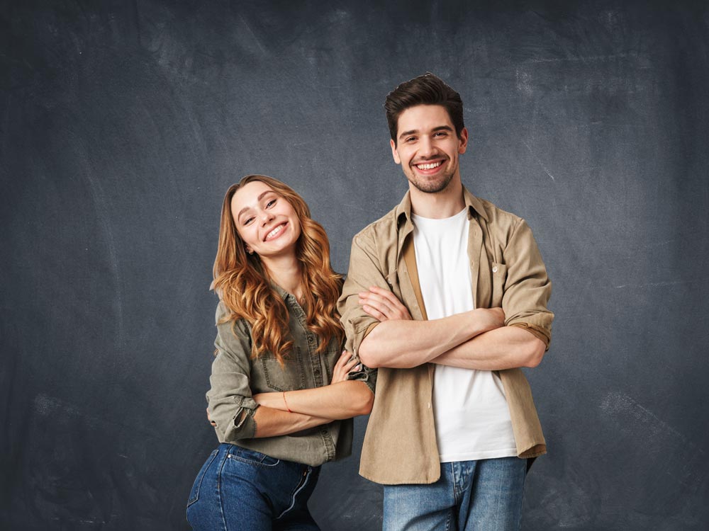 Ein Mann und eine Frau posieren selbstbewusst vor einem dunklen Hintergrund.