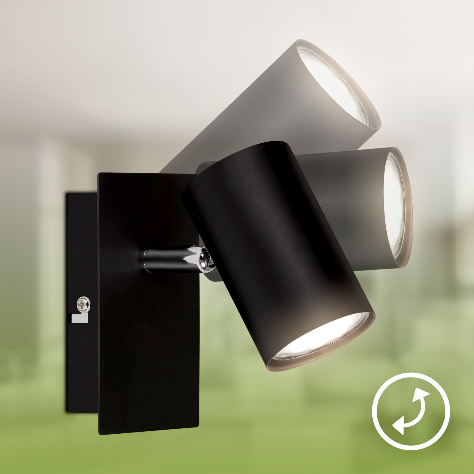 Close-up in driekwartaanzicht van een moderne zwarte wandlamp met drie verstelbare, cilindervormige spots tegen een onscherpe groene achtergrond