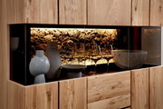 Moderne Holzvitrine mit Glasfront und warm beleuchtetem Steinrückwand-Design, dekoriert mit Keramikvasen, Schale und Weingläsern, Frontansicht leicht seitlich